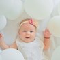 baby dressed in white surrounded by white balloons