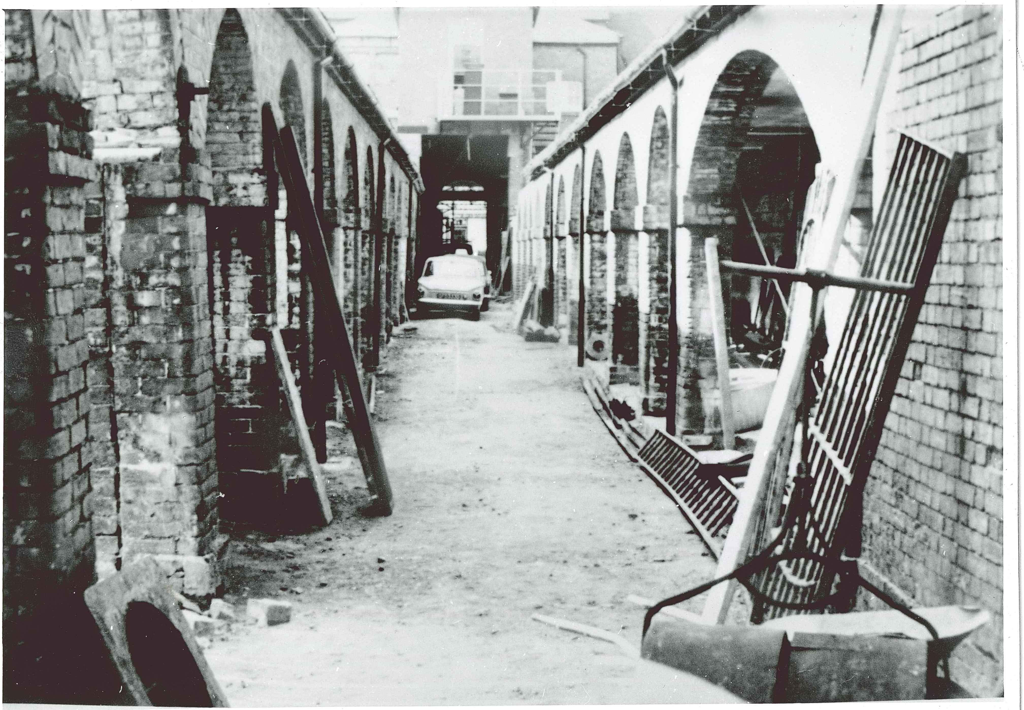 Old cobbled walkway surrounded on either side by brick archways and industrial machinery