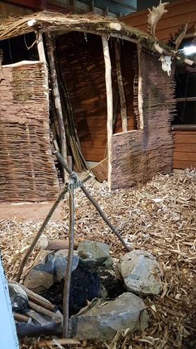 bronze age exhibition showing fire pit in foreground, entrance to hut in background