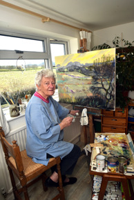 artist in home studio sat at easel with landscape painting on canvas