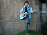 music performer leaning against a wall holding a guitar
