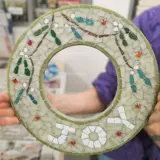 a circvular mosaic pieve in the theme of Chrsitmas with the words JOY written in mosaic tiles pieces