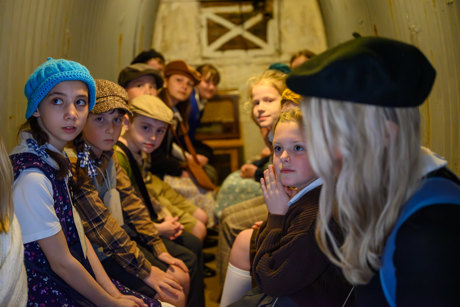 a group of children dressed in World War II clothing sat in an air raid shelter