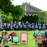 a brass band playing music with an audience seated in an outdoor theatre garden